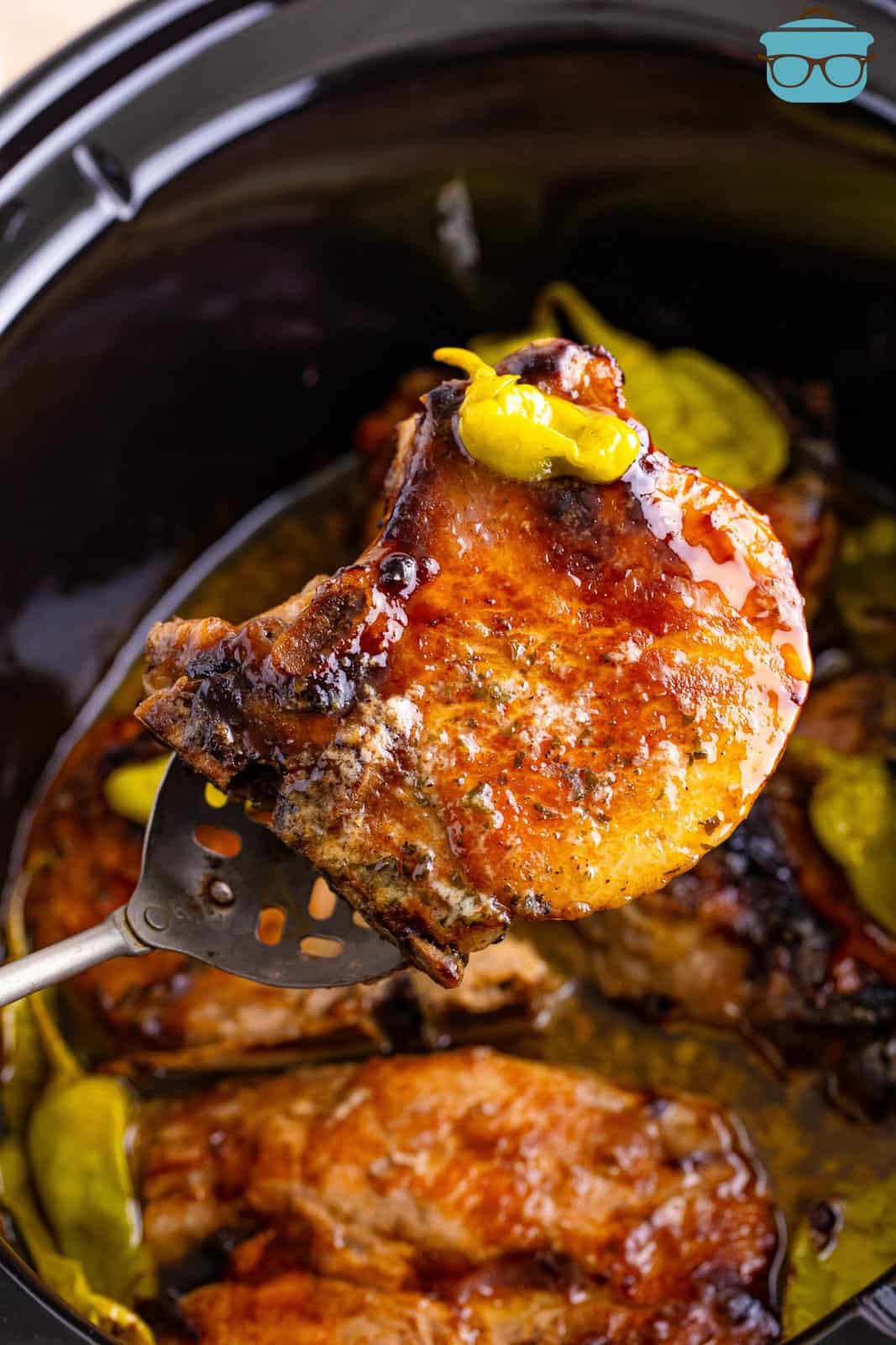 A serving utensil holding a pork chop above a crock pot.