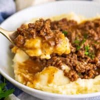 A utensil holding a big bite of Ground beef and gravy.