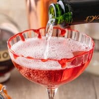 Square image close up of champagne being poured into glass for the Vampire's Kiss Cocktail.